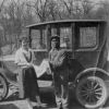 Woman and a mechanic pose in front of a 1920's era automobile