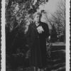 M. Bessie DeGraw in overcoat posing in front of a tree