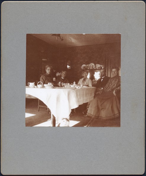 Bessie DeGraw sitting at a breakfast table with an unknown group of people