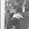 M. Bessie DeGraw sitting in wicker chair eating an apple