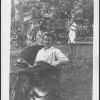 M. Bessie DeGraw sitting in wicker chair eating an apple, smiling at camera