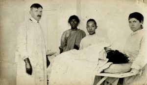 Man in surgical gown, next to patient on table with others in surgical gowns standing by to assist.
