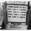 Two unknown men standing in front of the Battle Creek Tabernacle announcement sign