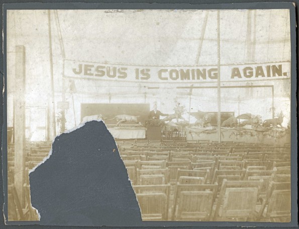 William Simpson posing with papier mache beasts on the podium inside a tent