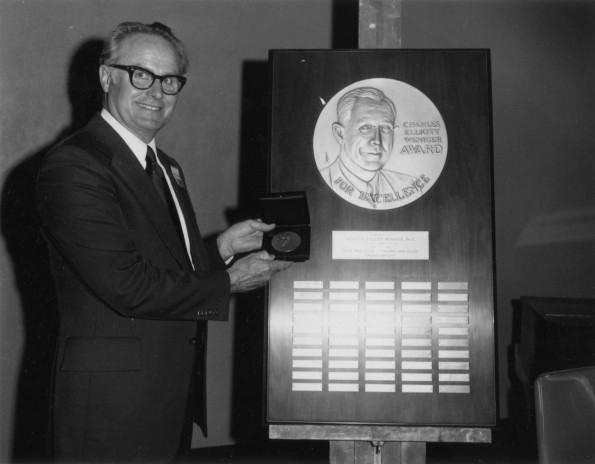 Clinton Emmerson is posing by Charles Elliot Weniger Award for Excellence plaque
