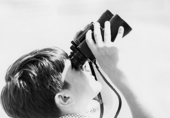 A boy using a binocular to watch the Andrews University aviation airshow performance