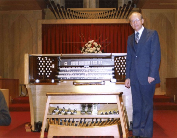 C. Warren Becker standing by new organ in Pioneer Memorial Church
