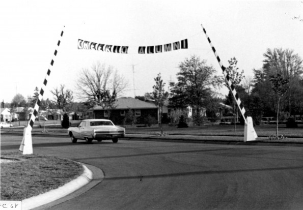Andrews University alumni leave campus after 1968 homecoming weekend by passing under a sign that reads, 'Cheerio Alumni', at the gate