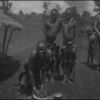 Kisii woman grinding grain while other natives look on