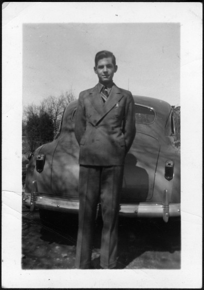 Young man in suit standing in front of a car, possibly Robert Sutherland